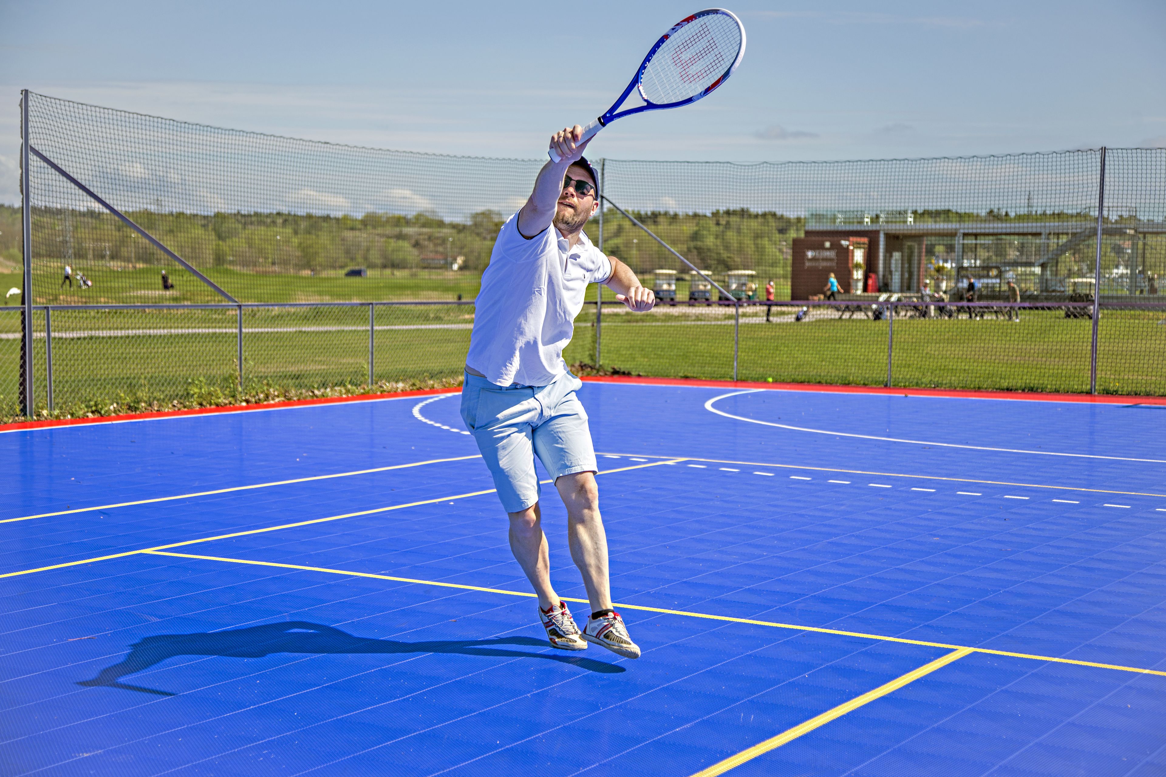Un court de tennis avec un filet, un joueur portant un t-shirt et un short blancs, et un ciel dégagé en arrière-plan.