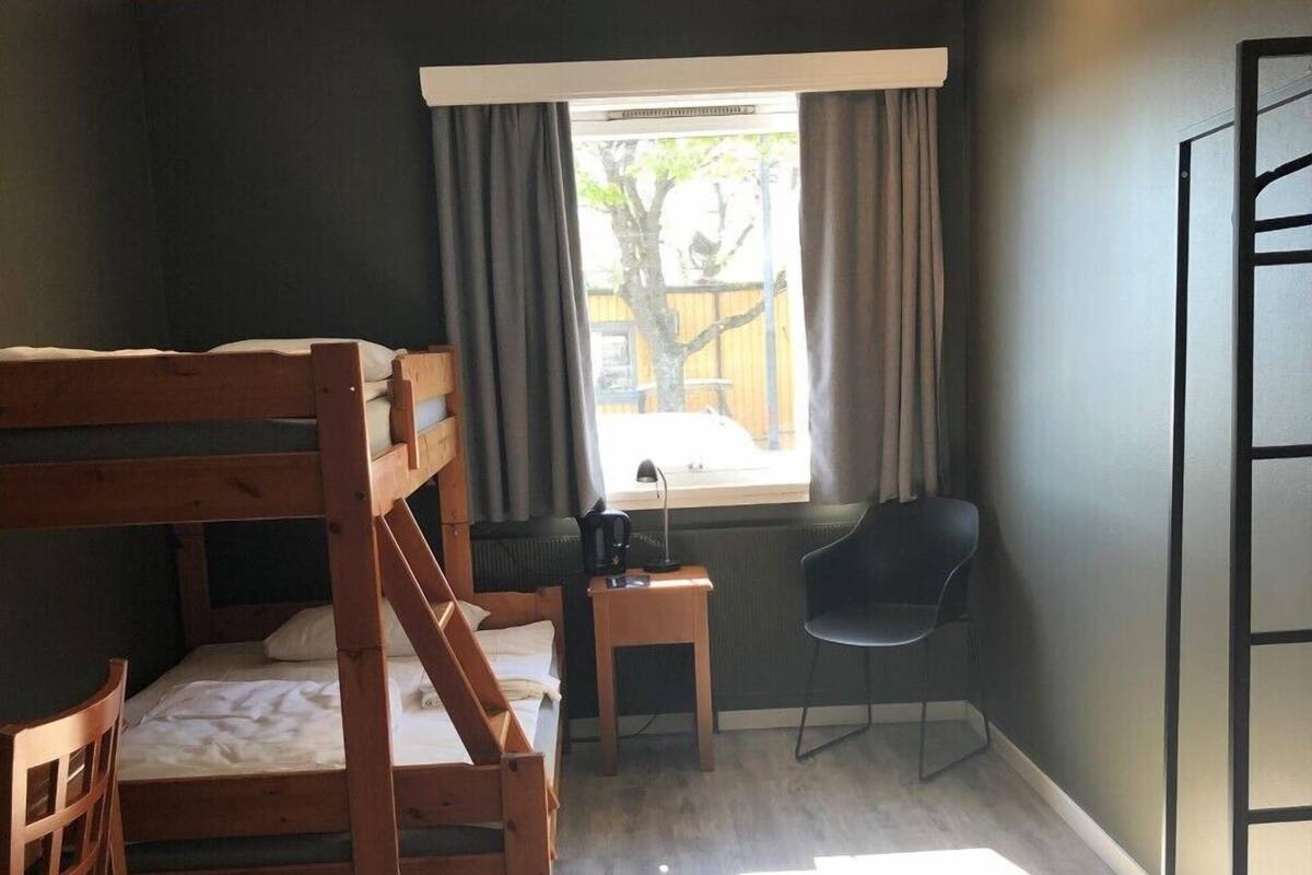 Une chambre avec un lit superposé, un bureau, une chaise et une fenêtre avec des rideaux.
