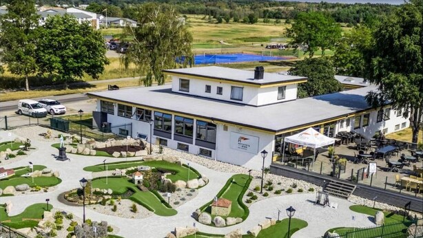 A modern building with a flat roof, surrounded by a landscaped garden with pathways and a small pond. - Aktivitetsbyen Gamle Fredrikstad (Fredrikstad)
