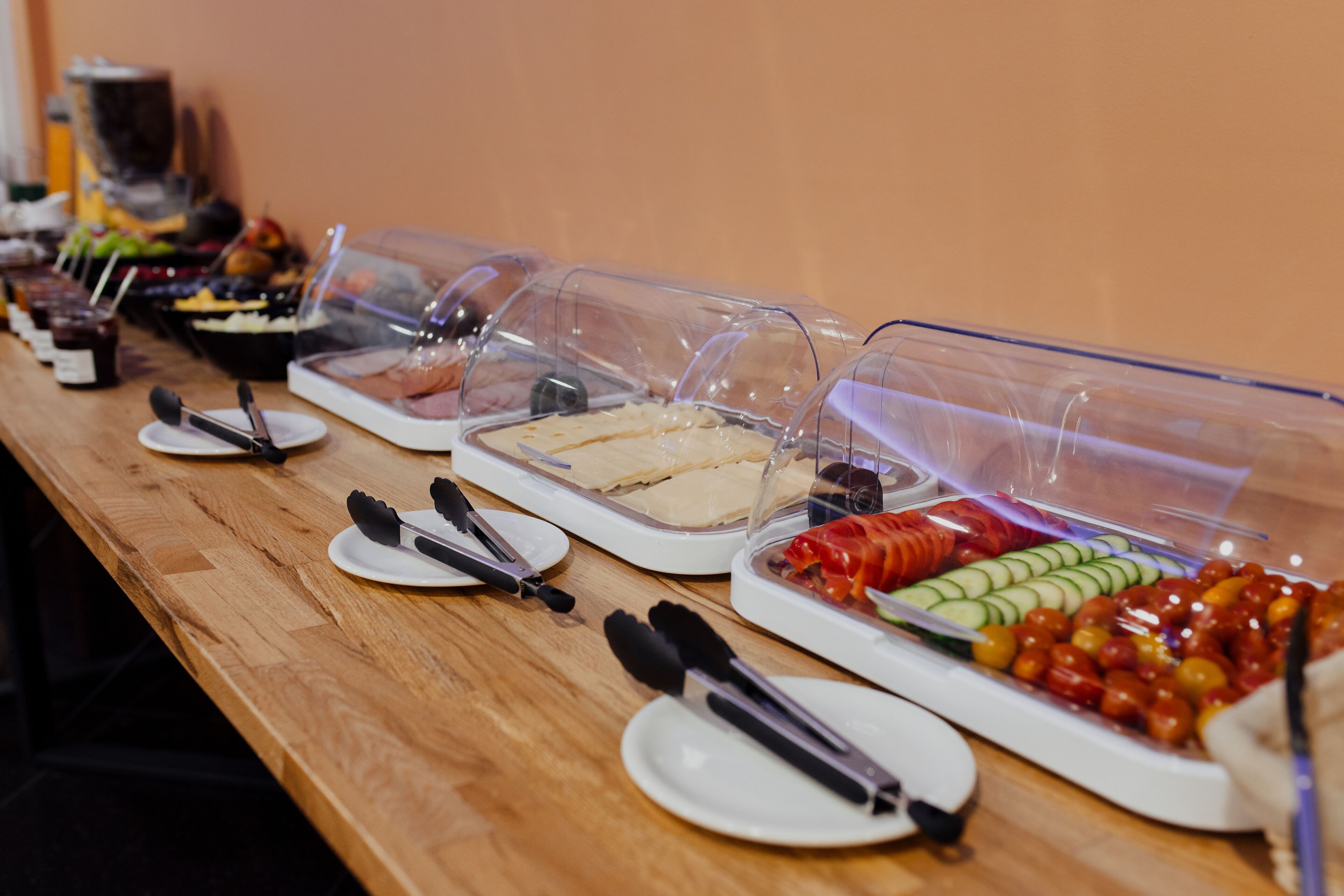 Ein Buffet mit verschiedenen Speisen, darunter Sandwiches, Obst und Gemüse, bedeckt mit Folie.