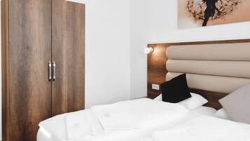 Un dormitorio con un armario de madera, una cama con ropa de cama blanca y una lámpara de pared.
