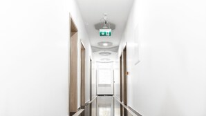 Un pasillo moderno y bien iluminado con un letrero de salida de emergencia verde, puertas de madera y un piso pulido.
