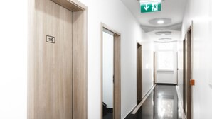 Un pasillo con puertas de madera, un cartel que indica la habitación 106 y una señal de salida de emergencia en el techo.