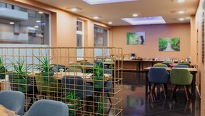 Un comedor moderno con un arreglo de plantas central, diversas opciones de asiento y vistas de la ciudad a través de amplias ventanas.