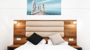 Una cama bien hecha con tablero de madera, dos mesitas de noche y un cuadro colgado en la pared de un muelle.