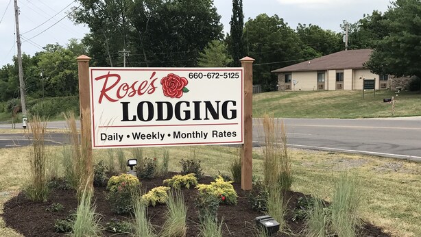 Señal de Rose's Lodging que muestra un número de contacto y ofrece tarifas diarias, semanales y mensuales.