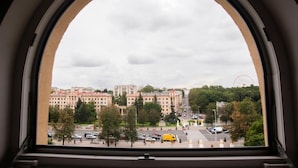 Vista a través d'una finestra d'arc, que mostra un paisatge urbà amb edificis, una noria i una zona d'aparcament.