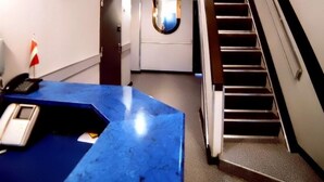 Zona d'eixida d'hotel amb un taulell de marbre blau, una escala i una finestra circular a la paret.