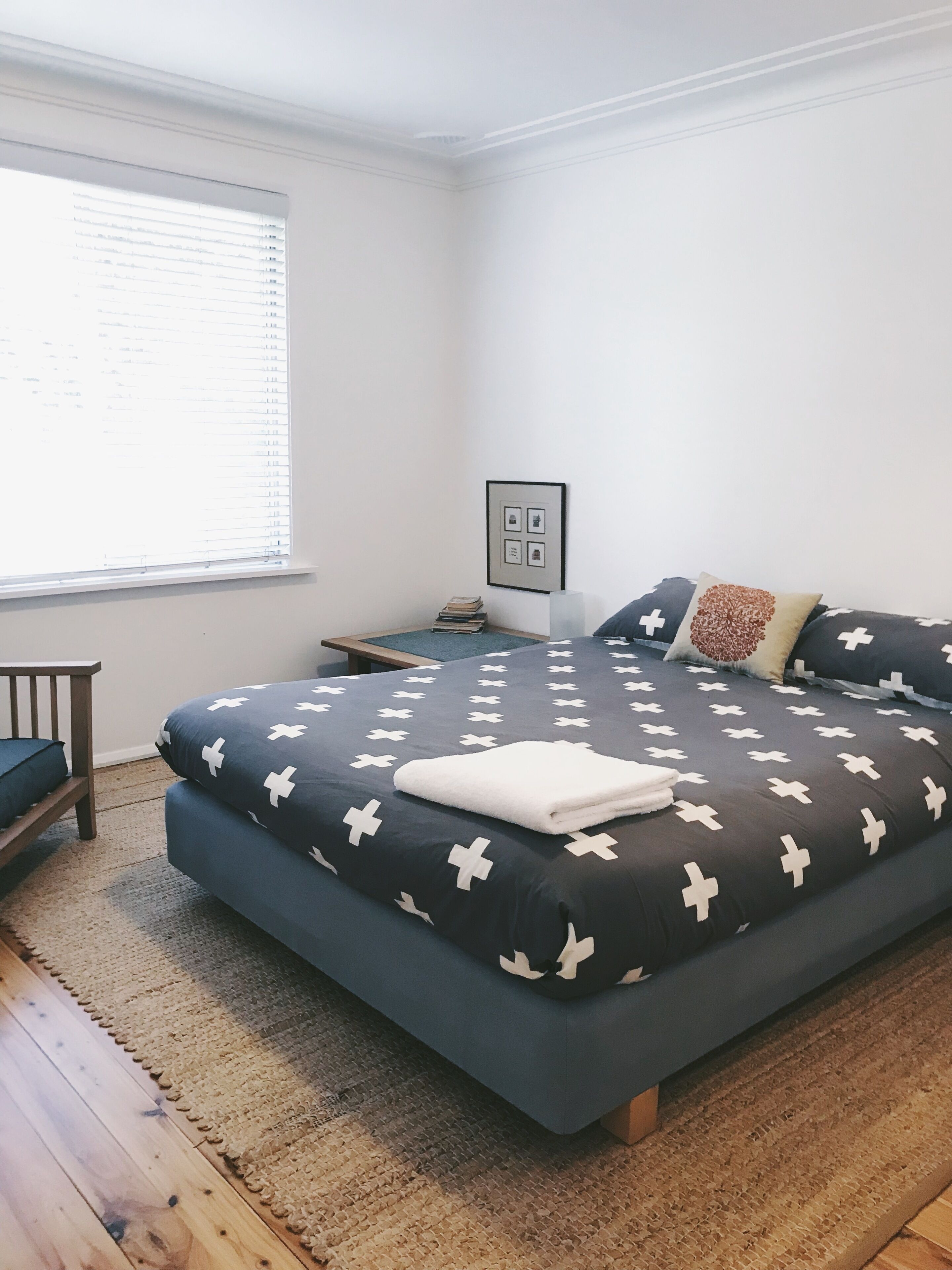 Una camera da letto con un letto, un comodino, una sedia, una finestra con persiane e un quadro appeso al muro.