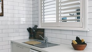 Una cocina moderna con armarios blancos, lavavajillas integrado, una ventana con persianas blancas y una tabla de cortar de madera en la encimera.