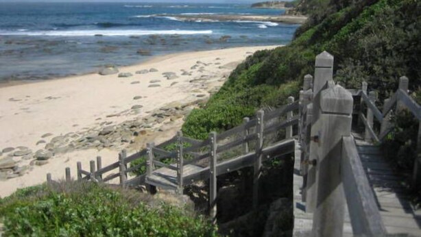 Un camino costero que lleva a una playa con valla de madera y terreno rocoso.