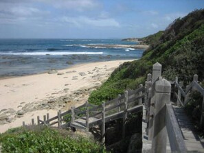 A coastal walkway leading to a beach with a wooden fence and rocky terrain.