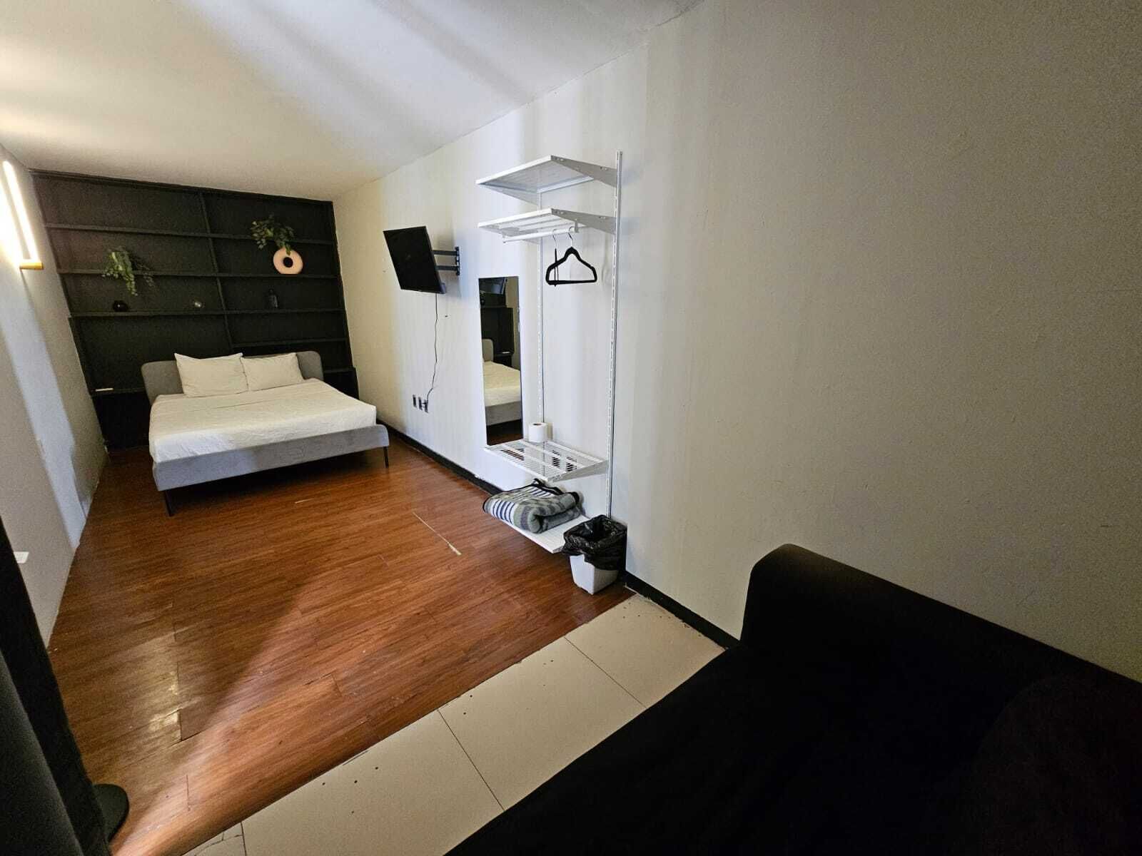 Un dormitorio moderno con cama, espejo, televisor y una pequeña zona de estar.