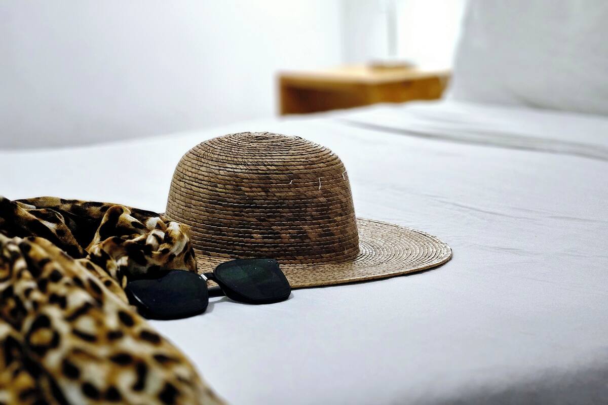 A bed with a woven hat and sunglasses on it.