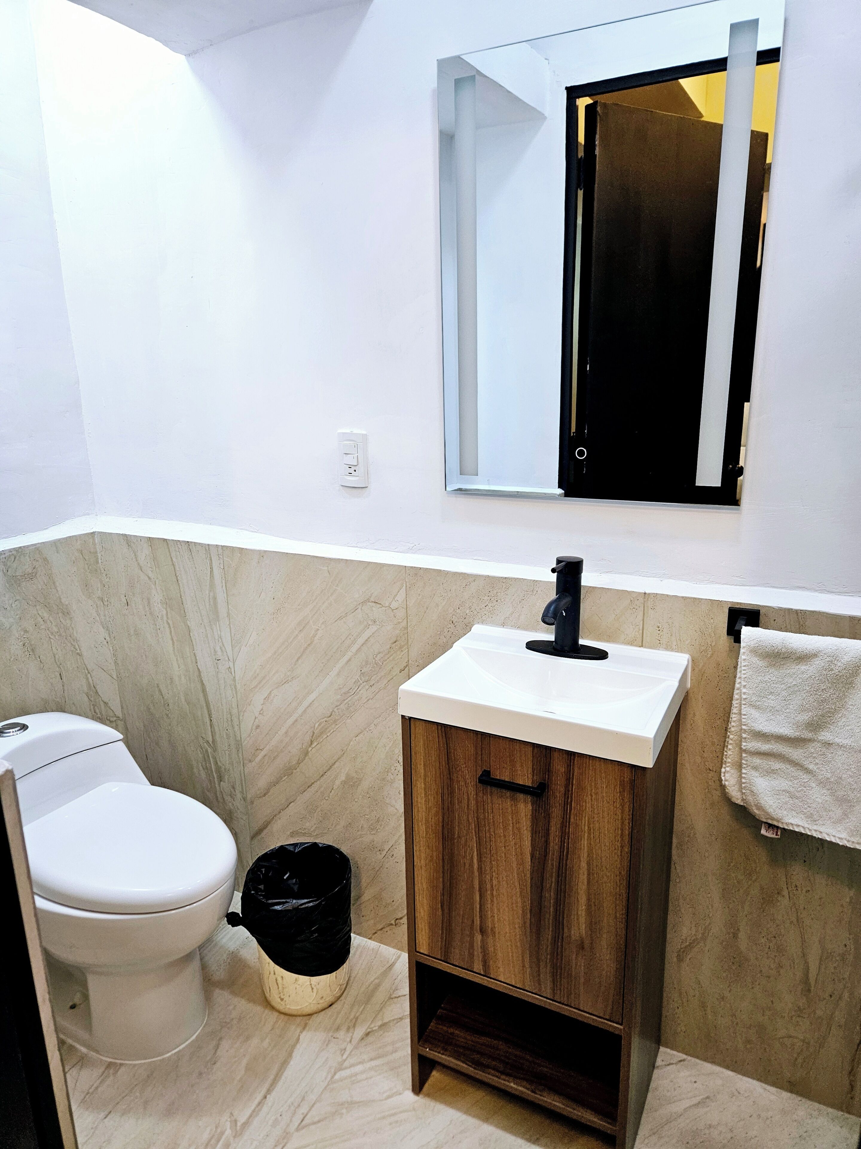 A bathroom with a toilet, sink, mirror, and a towel rack.
