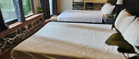 A hotel room with two beds, a stone wall, a desk with a lamp, and artwork on the wall.