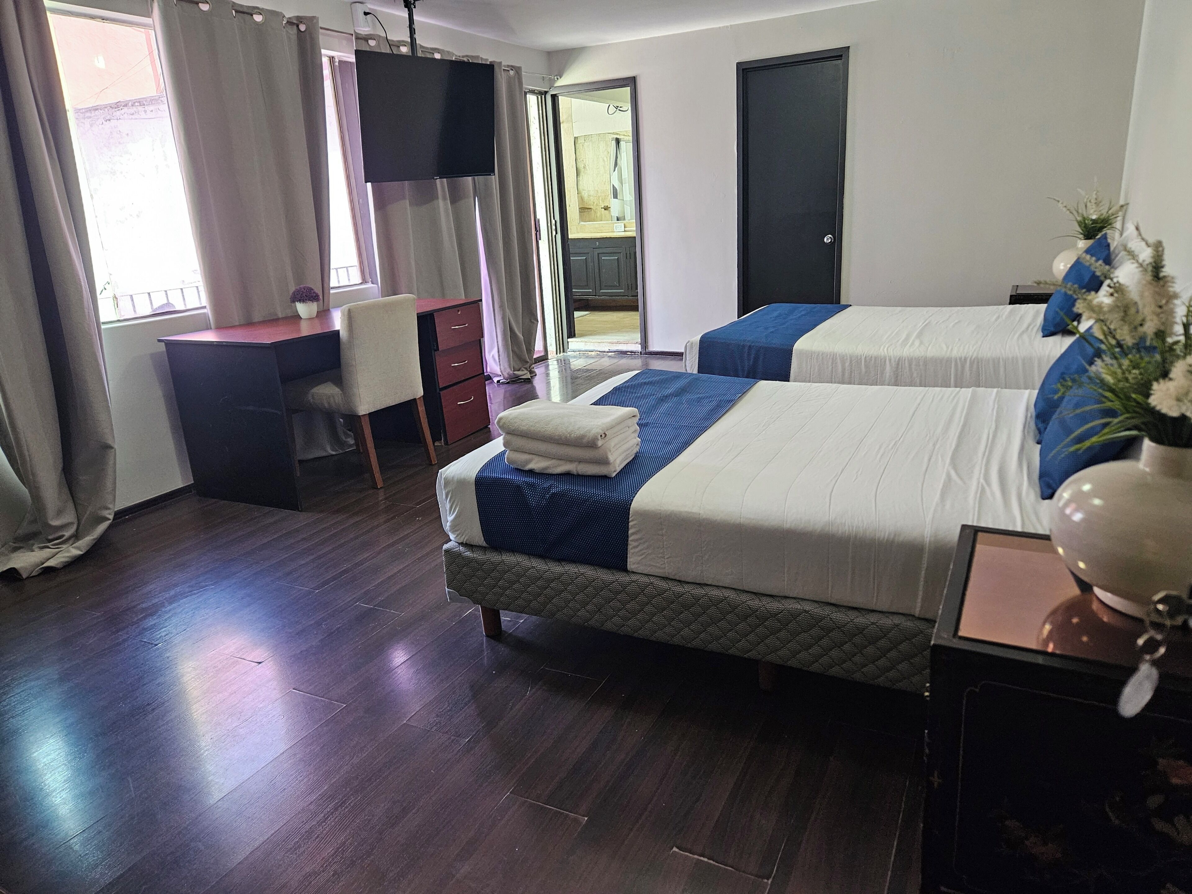 A hotel room with two beds, a desk, a chair, a TV, and a door.