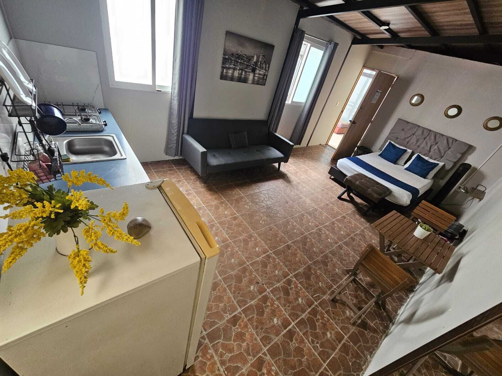 Ein gemütliches Zimmer mit Küchenzeile, einem Bett mit blauer Bettwäsche, einer Couch und einer Essecke mit kleinem Tisch und Stühlen.