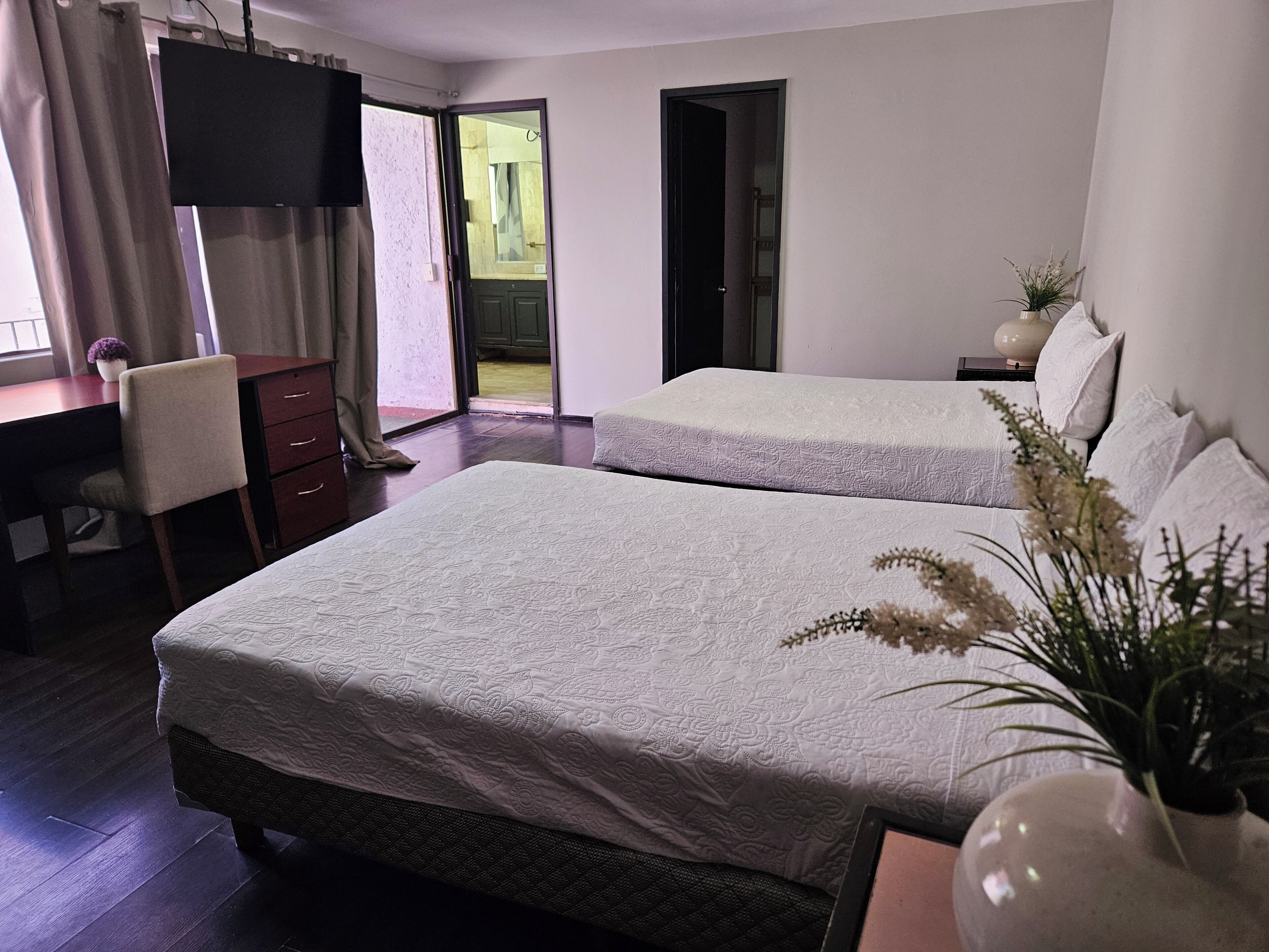 A hotel room with two beds, a desk, a chair, a TV, and a view of a courtyard.