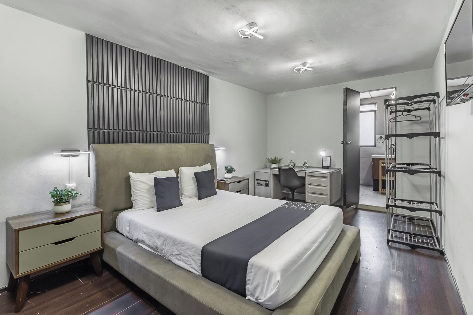Une chambre à coucher moderne comprenant un lit, des tables de chevet, un bureau, une chaise, une armoire et un porte-manteau.