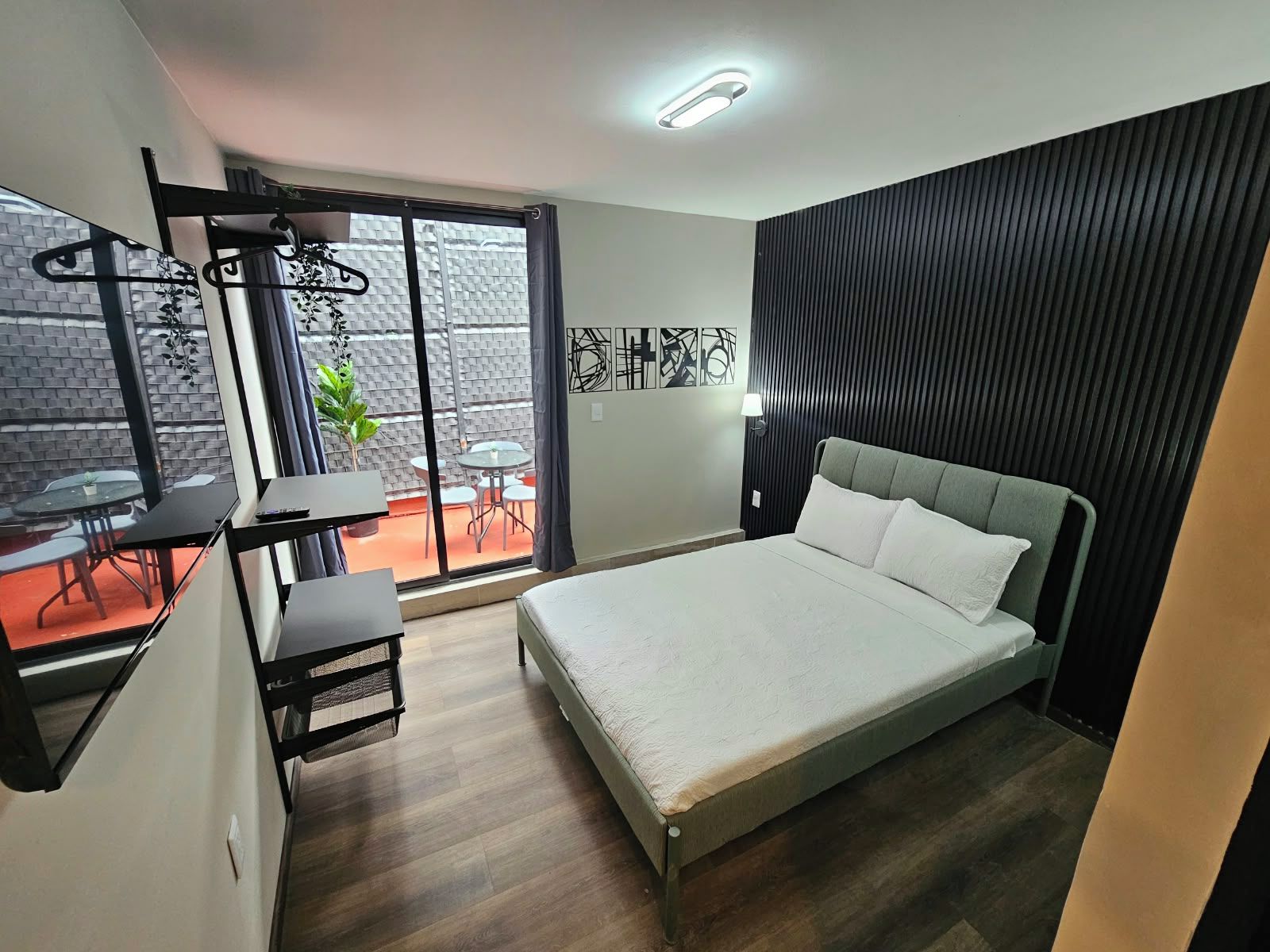 A modern hotel room with a bed, a desk, and a balcony with a table and chairs.