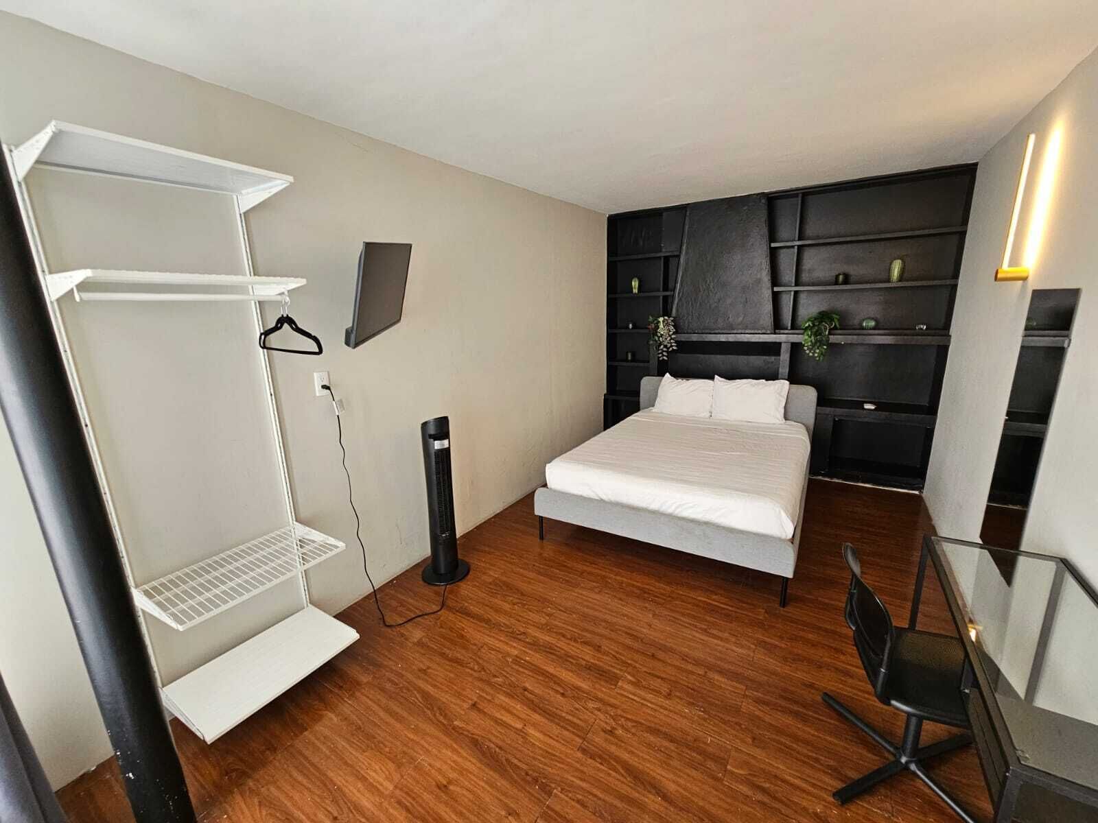 A modern bedroom with a bed, a desk, a chair, a wardrobe, and a shelf unit.