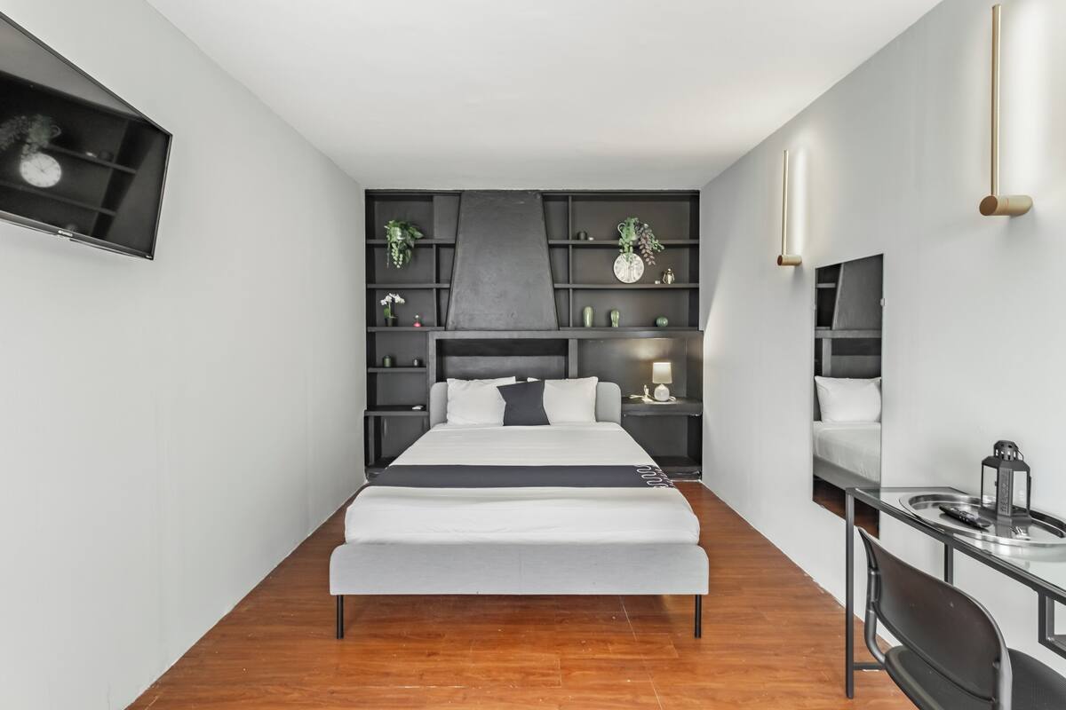 A modern bedroom with a bed, bedside tables, a desk, and built-in shelving.