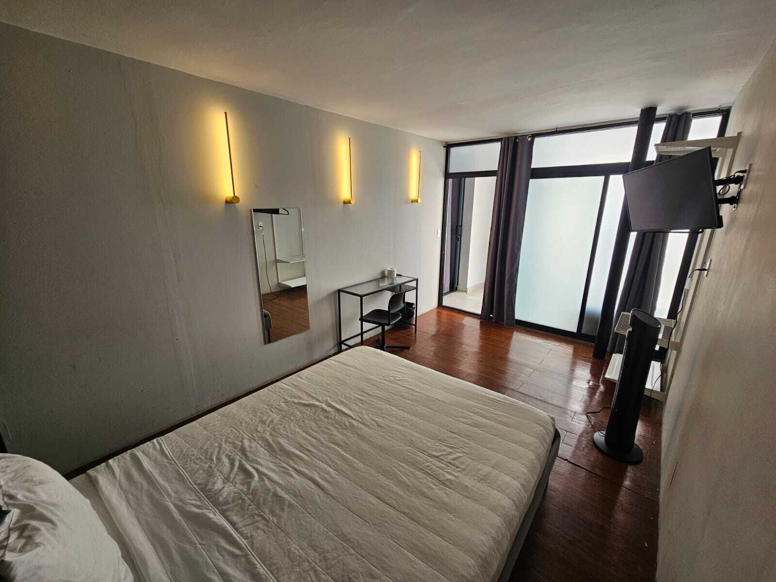 Une chambre d’hôtel avec un grand lit, un bureau, un miroir et une télévision.