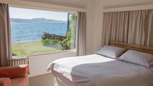 A bedroom with a large window overlooking a body of water, a bed, and a chair. - Absolute lakefront holiday house (Two Mile Bay (2 Mile Bay))