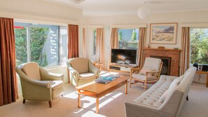 A spacious living room with a fireplace, comfortable seating, a flat-screen TV, and large windows offering a view of greenery outside. - Absolute lakefront holiday house (Two Mile Bay (2 Mile Bay))