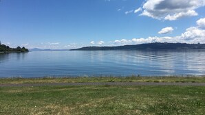 A calm lake with a clear sky, a grassy shoreline, and distant hills. - Absolute lakefront holiday house (Two Mile Bay (2 Mile Bay))