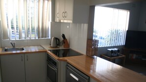 Cocina compacta con fregadero, estufa y lavavajillas, encimeras de madera y una ventana con persianas.