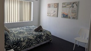 Un dormitorio con cama, ventilador de techo, ventana con persianas y dos obras de arte en las paredes.