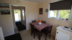 A dining area with a table set for four, a bowl of fruit, and a window with a blind.