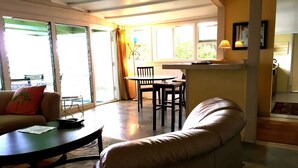 Sala de estar com sofá, mesa de jantar com cadeiras e cozinha com bancada e luminárias pendentes.