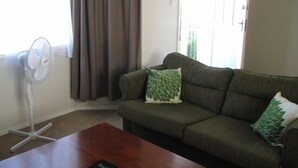 Un salon avec un canapé, deux coussins, un ventilateur et une table basse en bois.