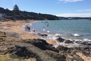 A beach with rocky shoreline, clear skies, and a few people in the water. - Koru Cottage - Pristine and newly renovated. (Paihia)