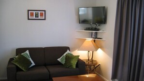 Un salon avec un canapé, une table basse, un téléviseur posé sur un meuble, une lampe et un cadre photo accroché au mur.