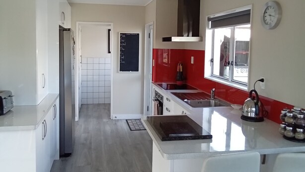 Cocina moderna con armarios blancos, una isla central con taburetes, un salpicadero rojo y una ventana con vistas.