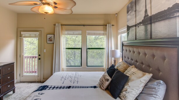 A bedroom with a bed, a ceiling fan, a window with curtains, a door, and a painting of the Eiffel Tower. - Whole Home Air Cleaner, Quiet surroundings, deck and Jacuzzi, near golf course (Austin)