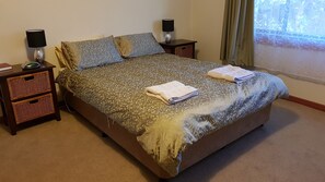 Ein ordentlich bezogenes Bett mit einem gemusterten Überwurf, zwei Kissen und je eine Nachttischlampe auf Holz-Nachttischen.
