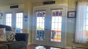 A cozy living room with a brown sofa, a glass coffee table, and two doors leading outside. - Breathtaking Remote Oceanfront Oasis Panoramic Clifftop Views (Lubec)