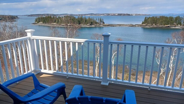 A deck with two blue Adirondack chairs overlooking a lake with a distant shoreline. - Breathtaking Remote Oceanfront Oasis Panoramic Clifftop Views (Lubec)