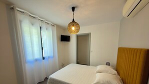 A bedroom with a bed, curtains, a hanging light fixture, a flat-screen TV, and an air conditioning unit. - Comfortable villa with heated pool and spa between sea and mountains (Aléria)