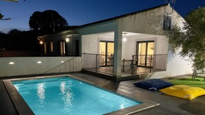 A rectangular swimming pool with a tiled deck, a covered outdoor seating area with tables and chairs, and a small building with a balcony. - Comfortable villa with heated pool and spa between sea and mountains (Aléria)