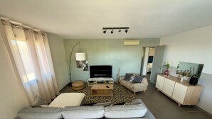 A modern living room with a grey sofa, a flat-screen TV, a coffee table, a patterned rug, and a cabinet with decorative items. - Comfortable villa with heated pool and spa between sea and mountains (Aléria)