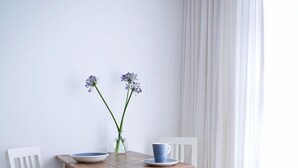 Una mesa de madera blanca con dos sillas, un florero con flores y una taza azul sobre la mesa.