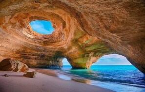 Een natuurlijke rotsformatie met een ronde opening, een zandstrand en de oceaan.