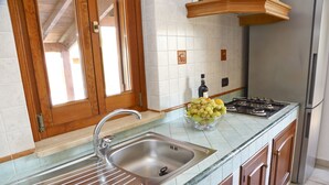 A kitchen with a stainless steel sink, a bowl of fruit, a gas stove, and wooden cabinets. - WELL-LIT MEDITERRANEAN VILLA WITH VERANDA AND GARDEN ONLY 50 METERS FROM THE SEA (Campofelice Di Roccella)