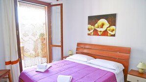 A neatly made bed with a purple bedspread and white pillows, a wooden headboard, a nightstand with a lamp, and a painting of flowers on the wall. - WELL-LIT MEDITERRANEAN VILLA WITH VERANDA AND GARDEN ONLY 50 METERS FROM THE SEA (Campofelice Di Roccella)